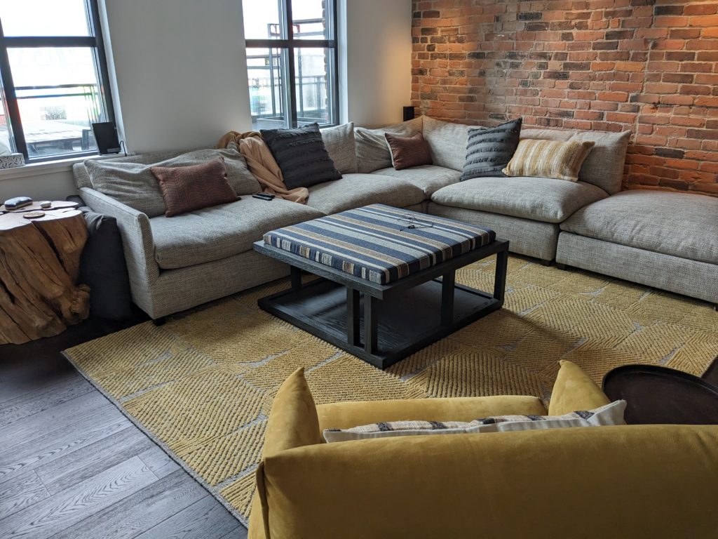 An oatmeal sofa against a brick wall, with a yellow chair in the foreground.